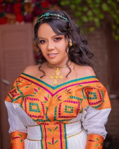 a woman in an orange and green dress with gold jewelry on her head is smiling at the camera