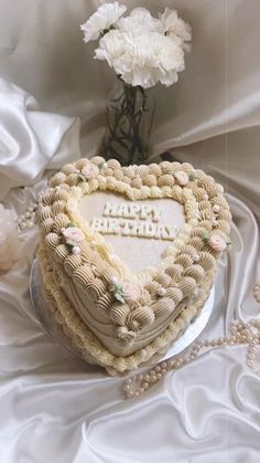 a heart shaped cake sitting on top of a table next to a vase with flowers