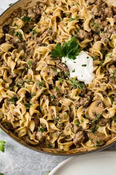 a skillet filled with pasta and meat covered in sauce, sour cream and parsley