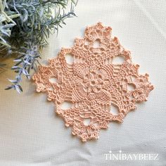 an orange doily sitting on top of a white table cloth next to a plant