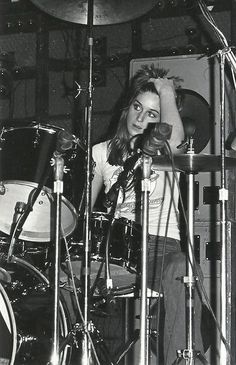 black and white photograph of a woman playing the drums in front of microphones on stage