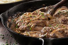 a skillet filled with meat and gravy on top of a wooden table