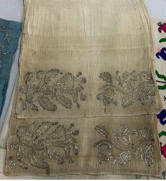 three pieces of cloth with embroidered designs on them, one is blue and the other is beige