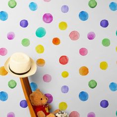 a teddy bear sitting on top of a chair next to a wall covered in multicolored polka dots