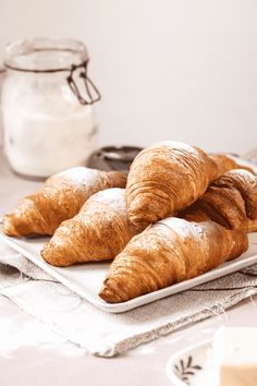 croissants on a white plate next to a jar of milk and spoon