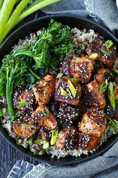 a black bowl filled with rice and meat covered in sesame seeds, broccoli