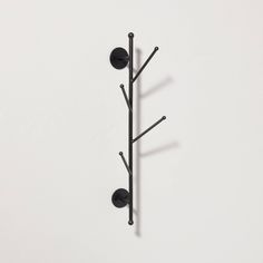 a black coat rack with three balls and two poles on the top, against a white wall