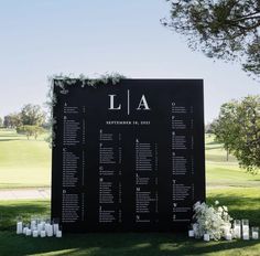 a large black sign sitting on the side of a lush green field next to candles