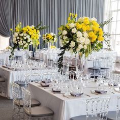 a long table is set with clear glasses and yellow flowers in vases on the tables