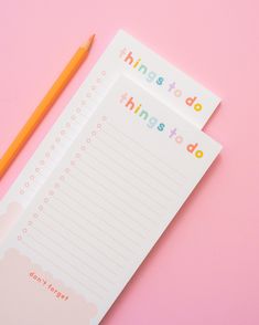 two notebooks sitting next to a pencil on top of a pink surface