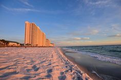 the beach is covered in white sand and blue water as the sun sets over the ocean