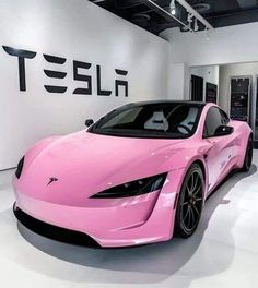 a pink sports car parked in front of a tesla sign