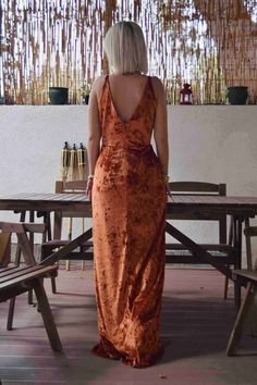 a woman in an orange dress is standing at a picnic table and looking out into the distance