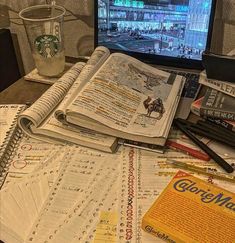 a laptop computer sitting on top of a table covered in books and papers next to a cup