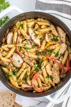 pasta with chicken and peppers in a skillet on a marble countertop next to bread