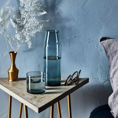 a table topped with glasses and vases next to a blue wall on top of a wooden table