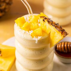 a pineapple and coconut smoothie on a white plate with honey in the background