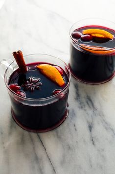 two glasses filled with liquid sitting on top of a marble counter topped with an orange peel