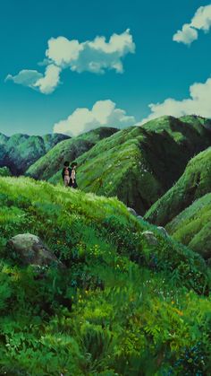 two people standing on top of a lush green hillside under a blue sky with clouds