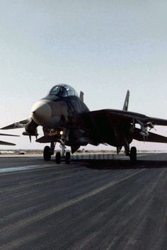 a fighter jet sitting on top of an airport tarmac next to another plane in the distance