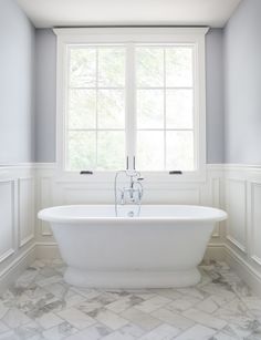 a white bath tub sitting next to a window in a bathroom with marble floors and walls