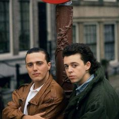 two men standing next to each other in front of a stop sign on a city street