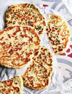 four flat bread pizzas sitting on top of a piece of wax paper covered in cheese