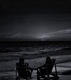 two people sitting in lawn chairs on the beach watching the sun set over the ocean