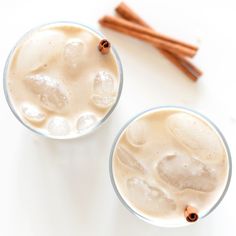 two cups filled with ice and cinnamon sticks on top of a white table next to each other