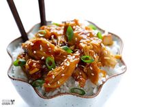 a white bowl filled with rice and chicken covered in sesame seeds, garnished with chopsticks