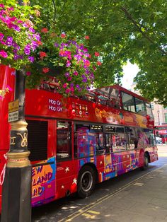 a red double decker bus parked on the side of the road next to a tree