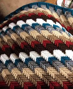 a crocheted blanket is laying on a table next to a cup and pen