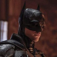 the dark knight batman is standing in front of a brick wall and looking off into the distance