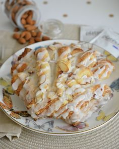 a white plate topped with pastry covered in icing next to nuts and almonds