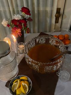 a table topped with a bowl of fruit next to a vase filled with oranges