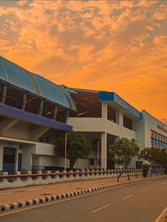 an empty street in front of a large building with a blue and white roof at sunset