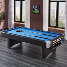 a pool table in the middle of a living room with large windows and hardwood floors