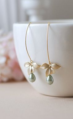 Matte Gold Orchid Flower Cream White Teardrop Pearls Long Dangle Earrings. Lovely matte gold flowers are hung from gold plated long oval hook ear wires with high quality 9mm x7mm Czech teardrop glass pearls dangling beneath. Pearls are in cream color. Flowers and ear wires are gold plated over brass. Total length of these earrings is approx. 2.5'' (64mm) including the long oval hook ear wires. These earrings are also available in silver finish here: www.etsy.com/lechaim/listing/243042921 ♥ Match Green Teardrop Pearl Earrings For Wedding, Elegant Flower Teardrop Earrings For Gift, Elegant Flower Shaped Teardrop Earrings, Delicate Teardrop Flower Earrings For Weddings, Green Drop Pearl Earrings For Wedding, Green Flower Earrings For Wedding, Elegant Green Flower Earrings For Wedding, Delicate Green Flower Earrings For Wedding, Bridal Jewelry Pearl Earrings