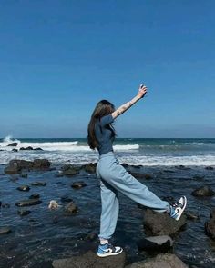 a woman standing on top of rocks near the ocean with her arms in the air