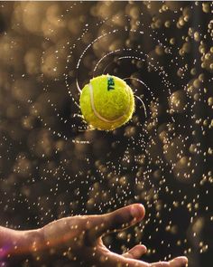 a tennis ball being tossed into the air by someone's hand with water droplets on it