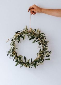 a hand holding a green wreath with white flowers and greenery hanging from the side