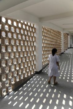 a woman walking down a hallway next to a wall with holes in it