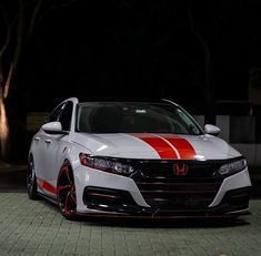 a white and red car parked in front of some trees at night with lights on