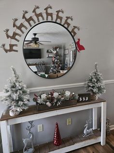 christmas decorations on a console table in front of a round mirror with reindeer silhouettes