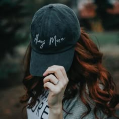 a woman with red hair wearing a black hat that says, always more on it