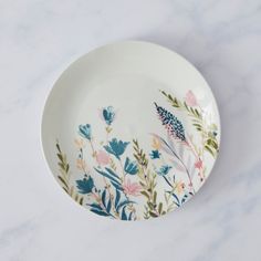 a white plate with flowers painted on it sitting on a marble countertop next to a knife and fork