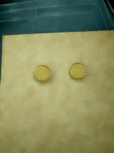 pair of yellow earrings sitting on top of a piece of paper next to a plastic container