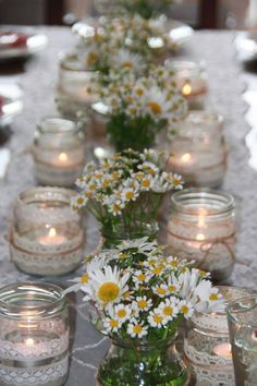 the table is set with mason jars and daisies in vases, candles and lace