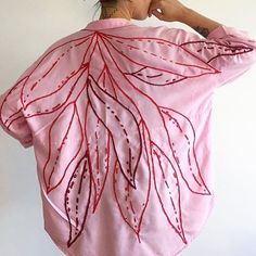 a woman wearing a pink shirt with red threadwork on the back and large leaves