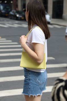 a woman is walking across the street with a yellow purse on her shoulder and she's looking back